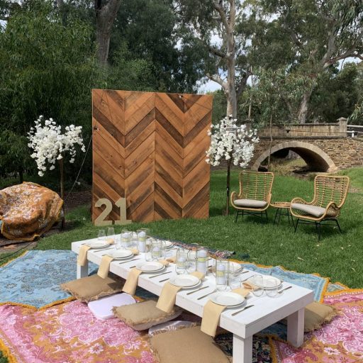 picnic-package-with-white-pallet-picnic-table-glass-candle-boxes-with-champagne-linen-napkins-AFC-crockery-and-standard-glassware-assorted-cushions-and-wandering-folk-rugs